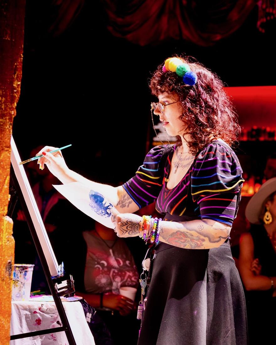 CeeCee painting live at Art Battle, wearing a rainbow pom-pom headband